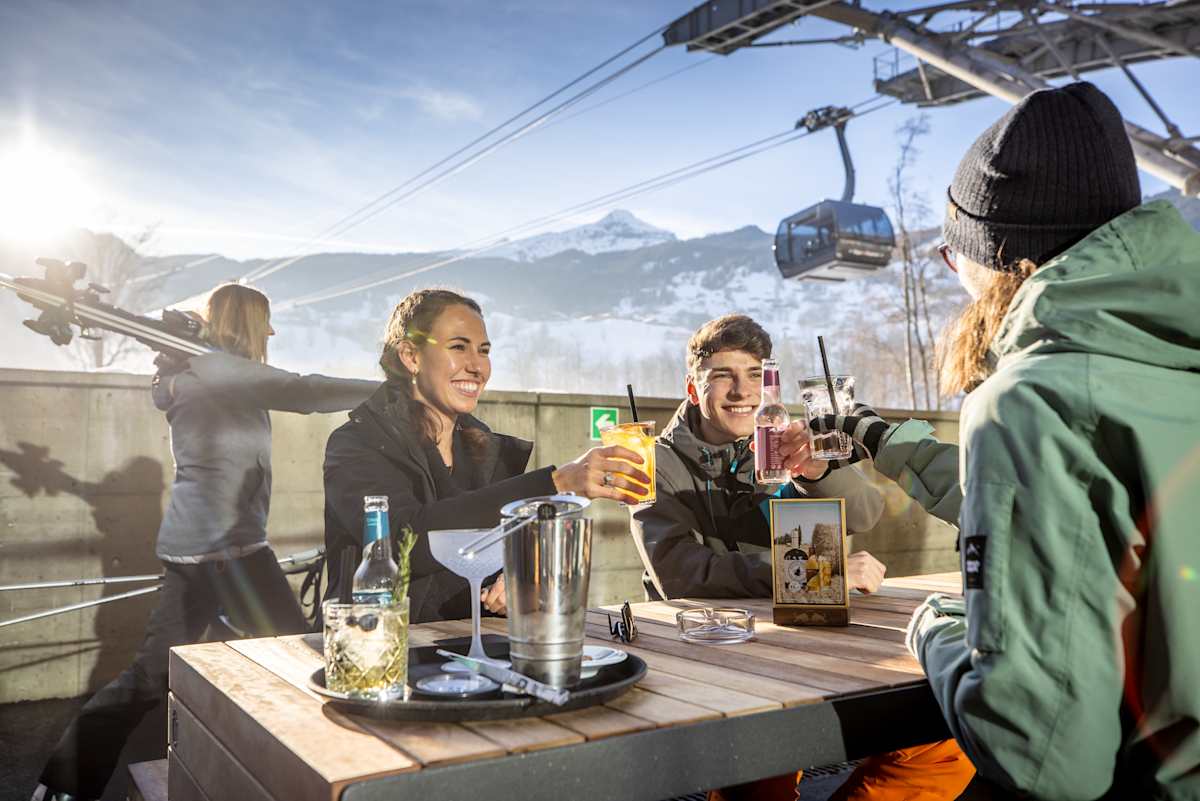 Vier Personen stossen im Aussenbereich der e-tron energy bar an, während eine Gondel des Eiger Express vorbeifährt.