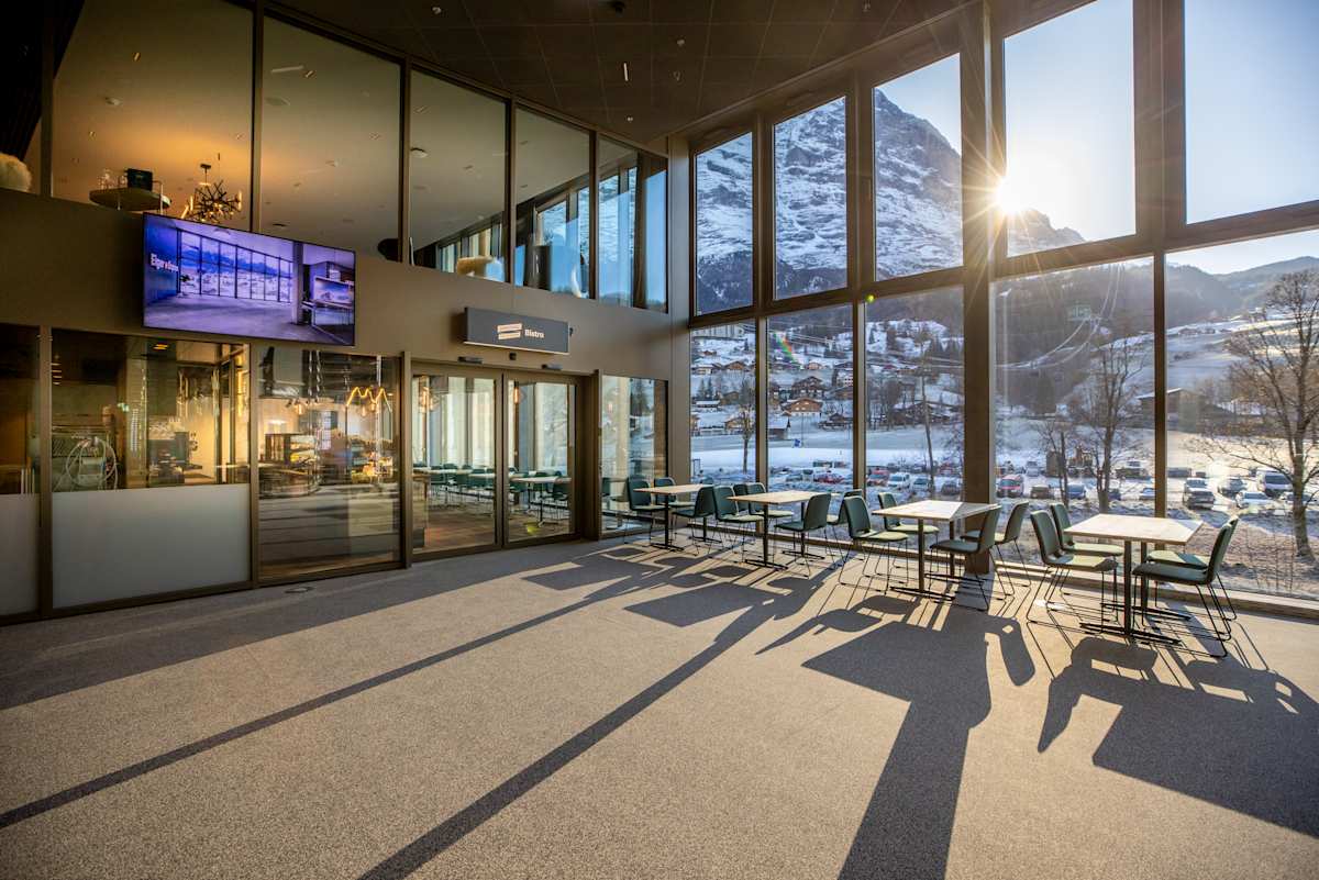 Sitzbereich des Bistros im Grindelwald Terminal mit Panoramafenstern und Blick auf den Eiger bei tief stehender Sonne.