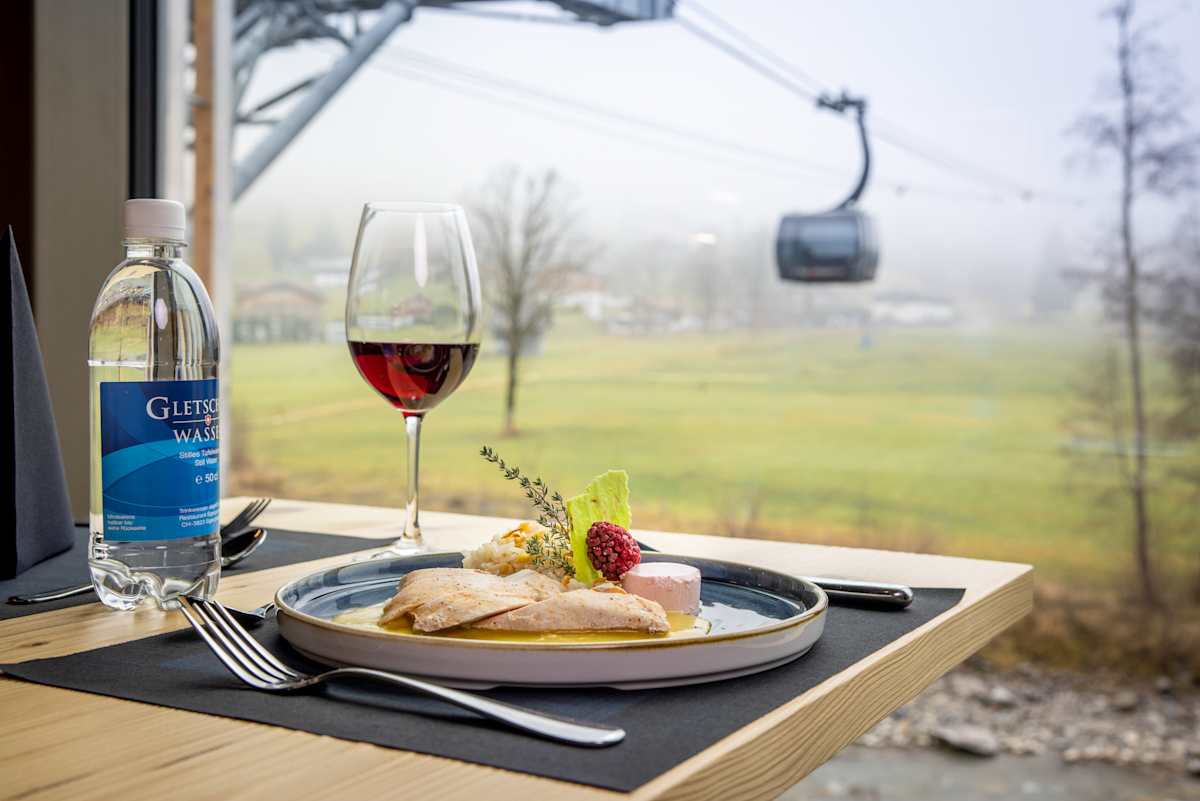 Angerichtetes Menü mit Rotwein und Blick auf eine Gondel des Eiger Express.