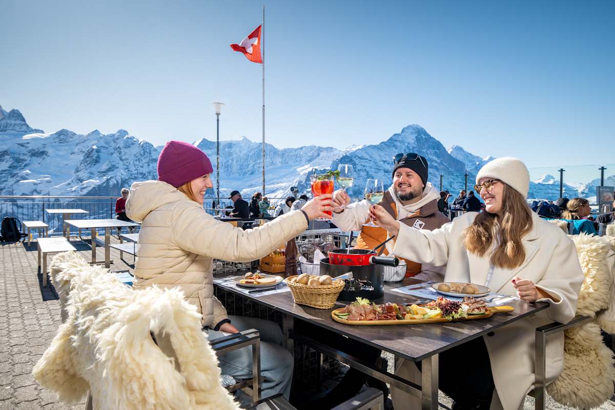 Drei Personen am anstossen auf der Terrasse des Berggasthaus First im Winter